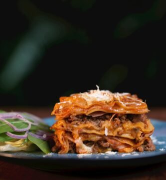 Lasaña clásica italiana recién horneada con capas de carne, bechamel y queso, acompañada de ensalada fresca