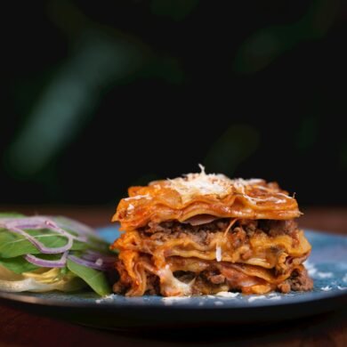 Lasaña clásica italiana recién horneada con capas de carne, bechamel y queso, acompañada de ensalada fresca